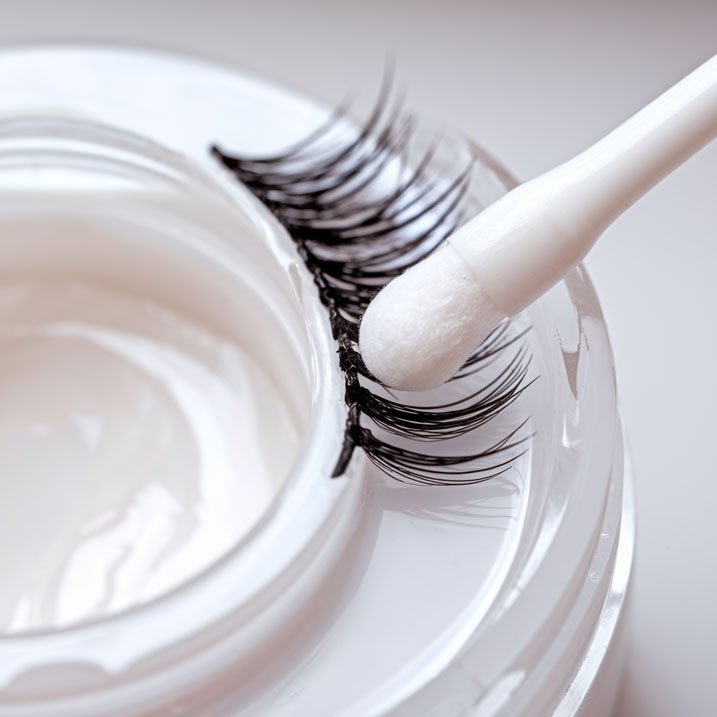 Applying gel remover to lash extensions using a cotton swab.