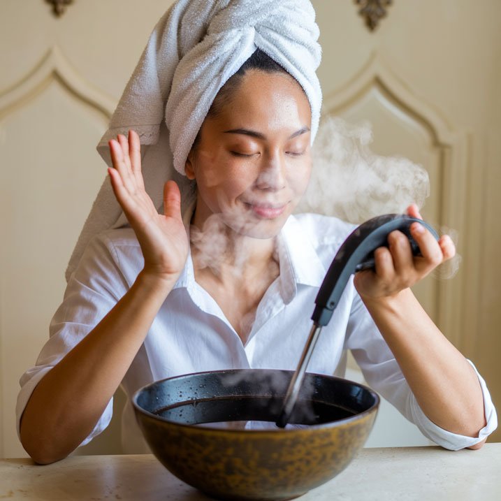 Woman steaming her face to soften lash extension glue for removal.